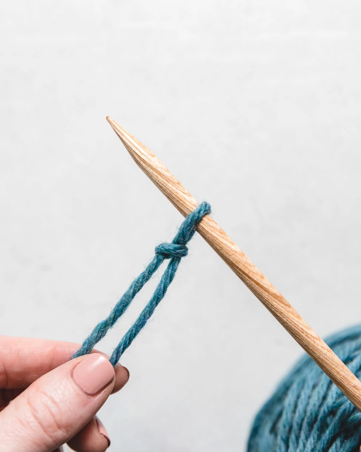 blue yarn and wooden knitting needle show how to do the knitted cast on