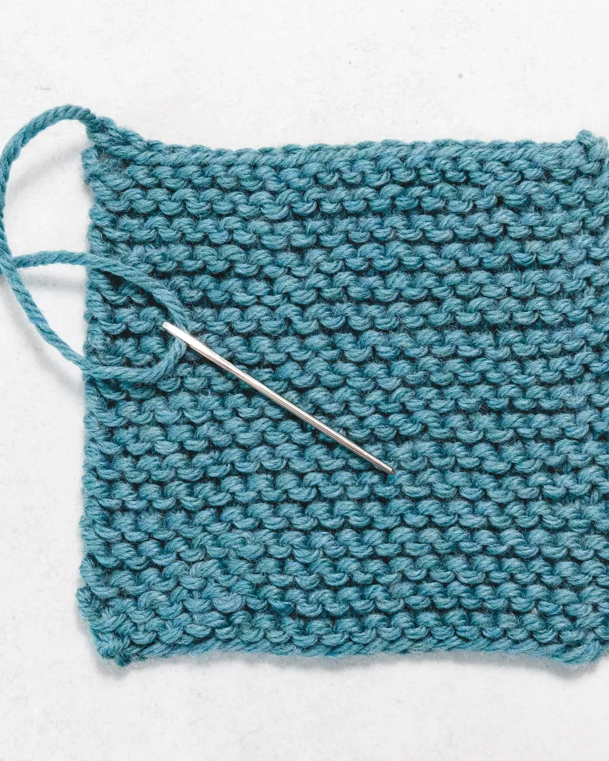 a swatch of garter stitch in blue yarn, with a metal tapestry needle