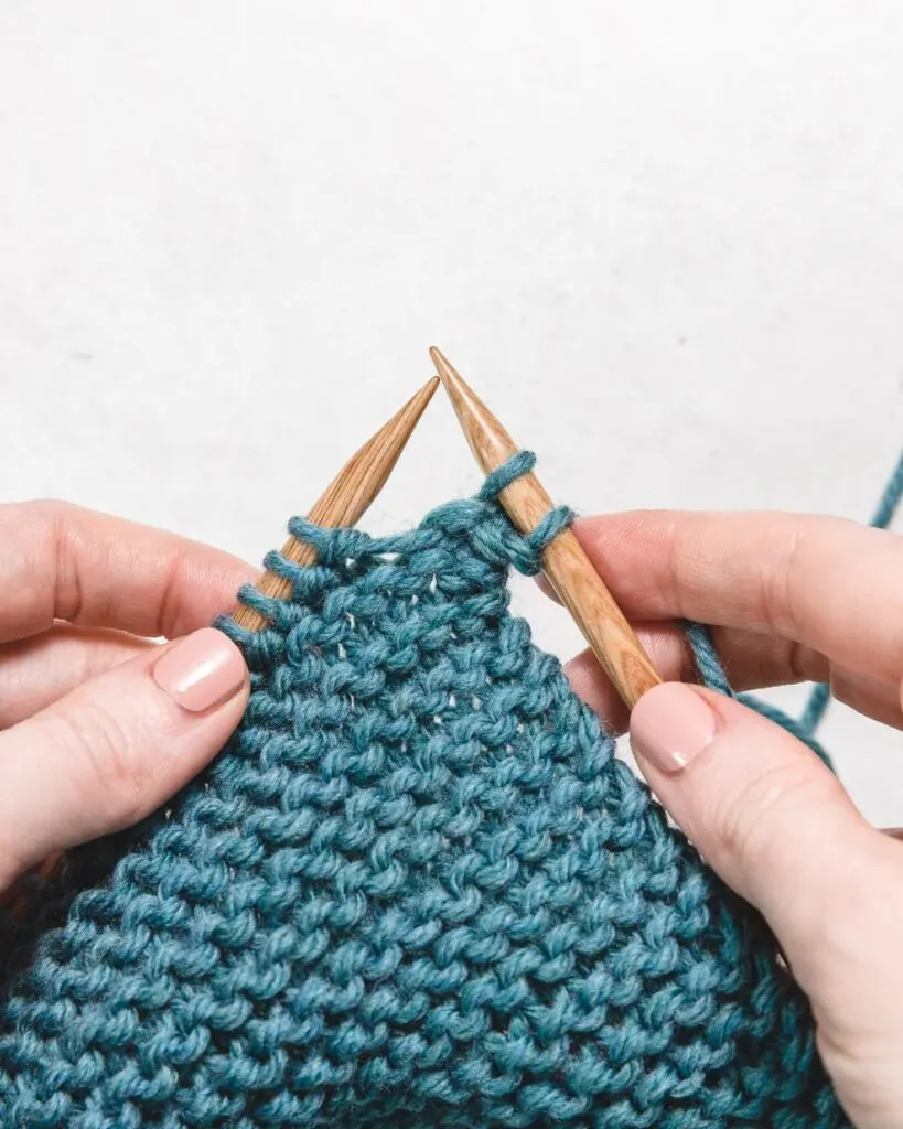 a swatch of garter stitch in blue yarn, with wooden knitting needles