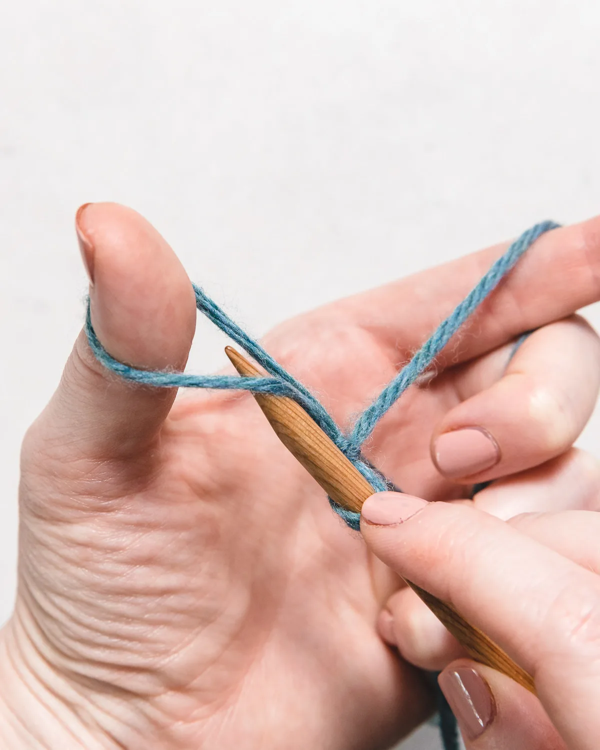 wooden knitting needle under the loop of yarn to make the first step of the long tail cast on