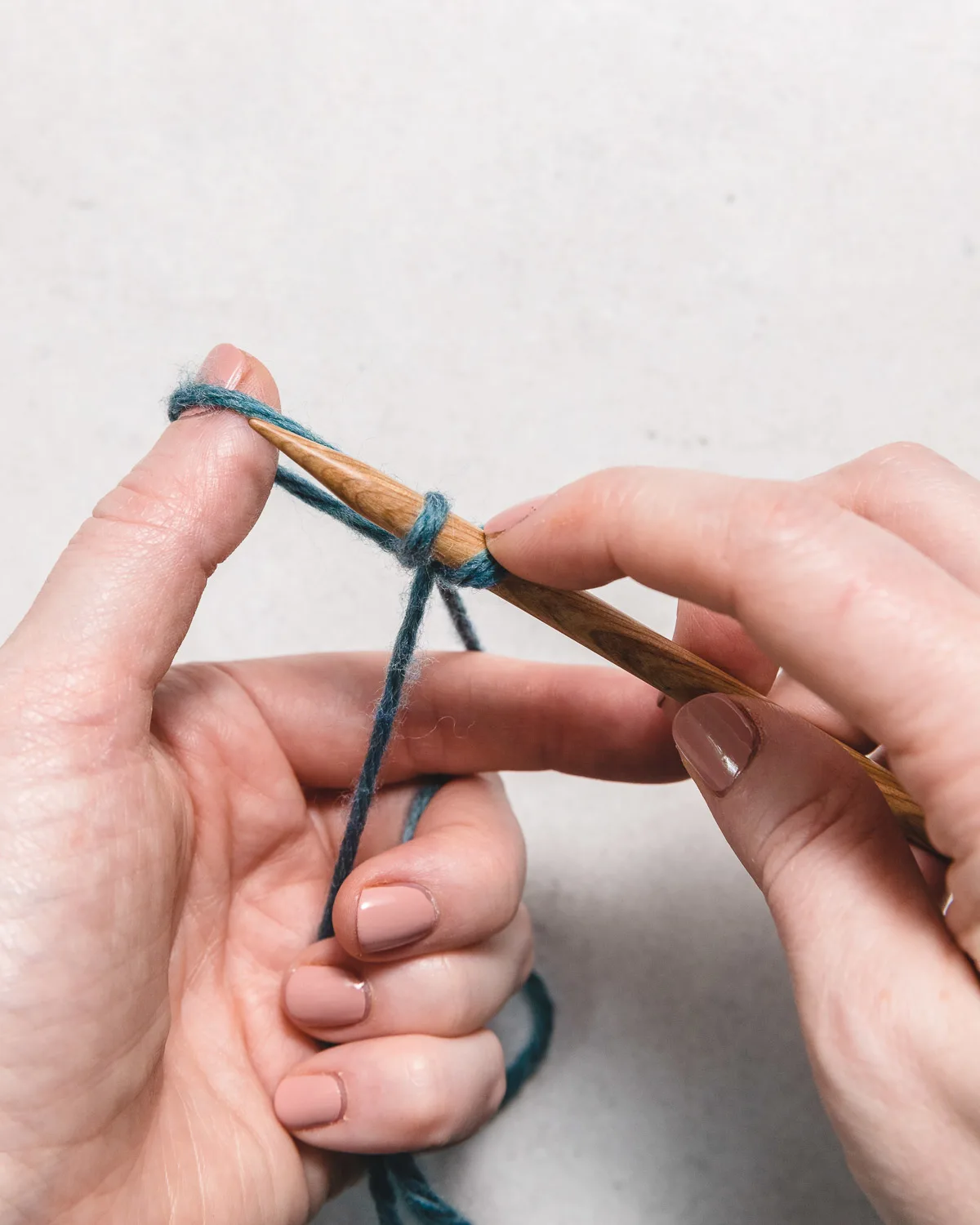 sliding the blue yarn off of the finger to tighten the cast on stitch on the wooden knitting needle