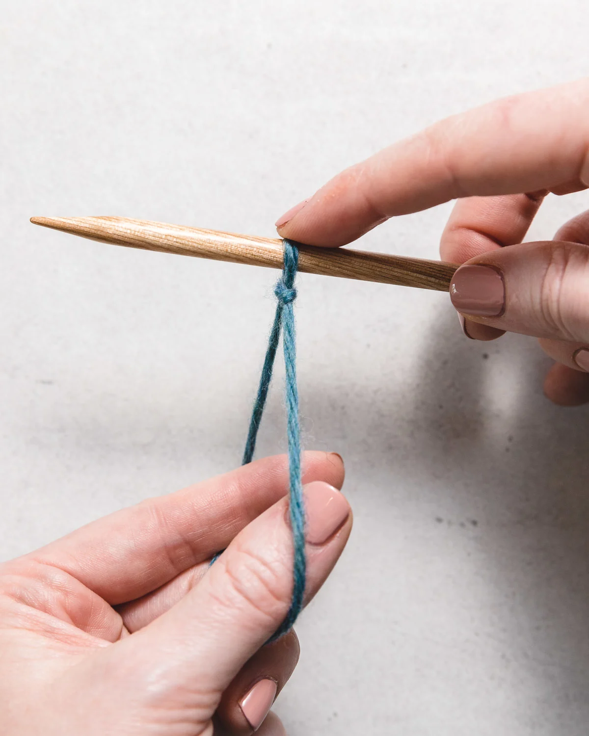 wooden knitting needles and blue yarn setting up the long tail cast on