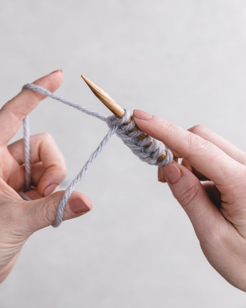 two hands holding one knitting needles casting on gray yarn