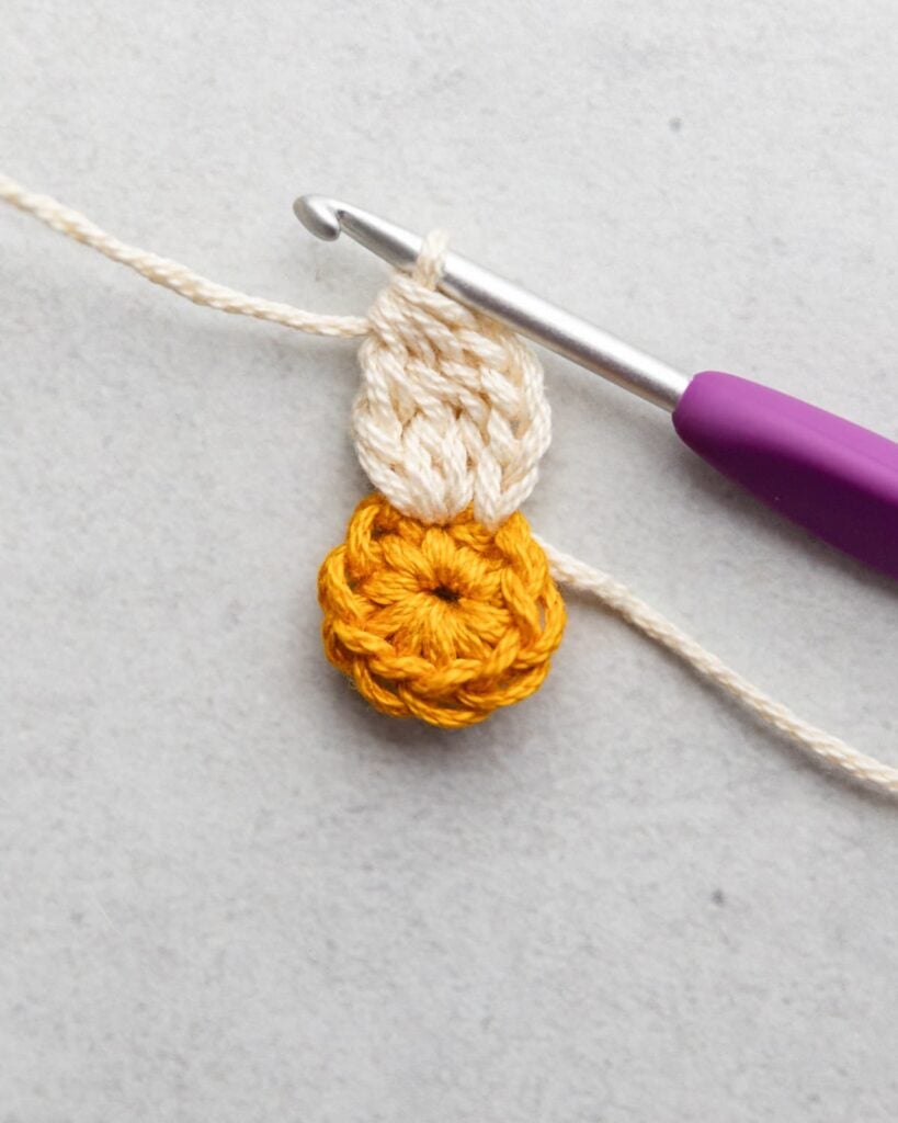 finishing the first petal of a crochet flower with a gray and purple crochet hook